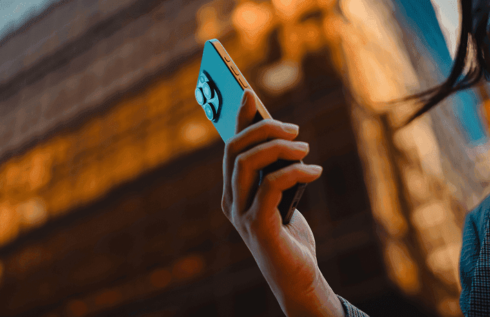 Person checking financial market data on a smartphone with trading charts in the background